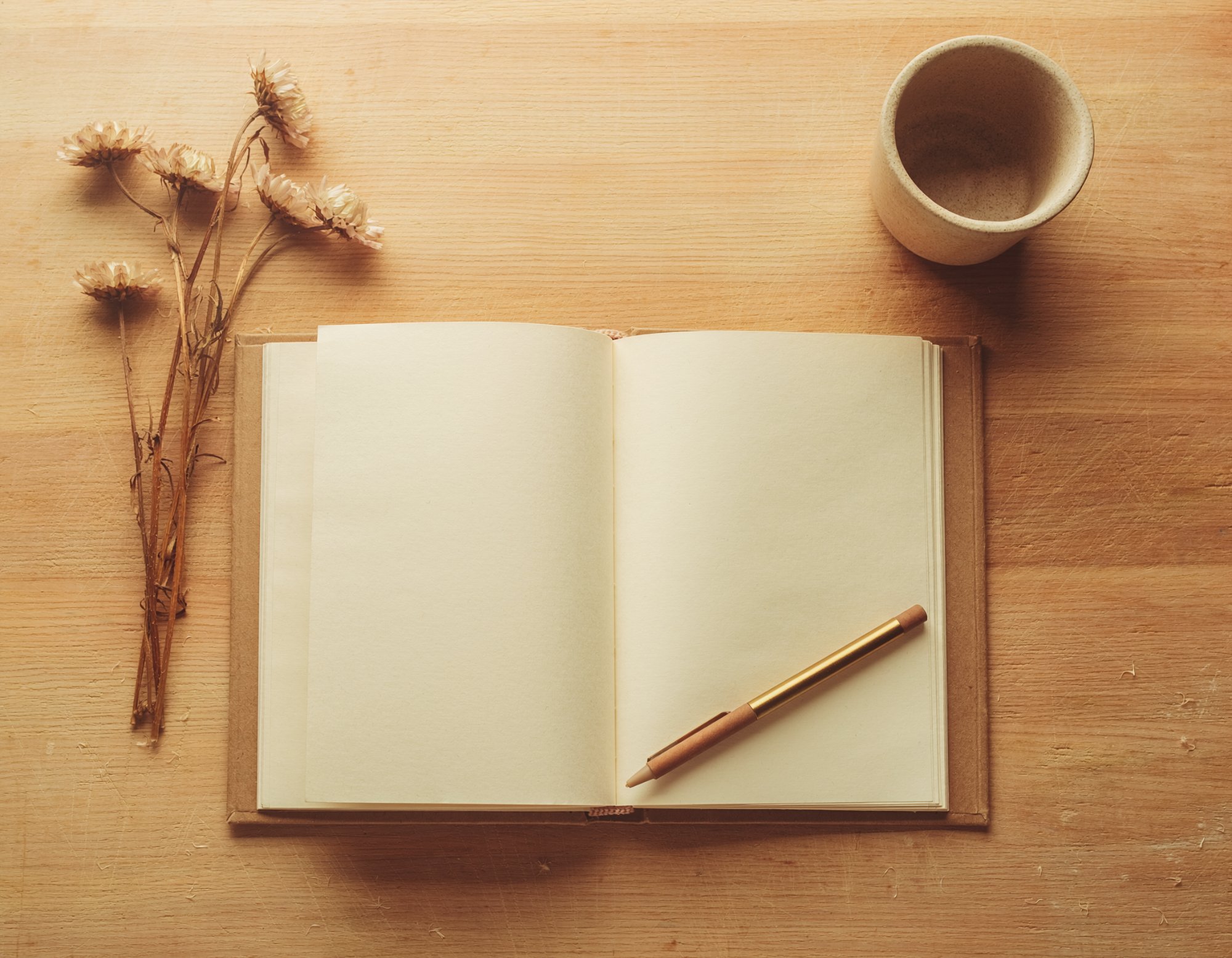 Open journal with pen and dried flowers on wooden desk